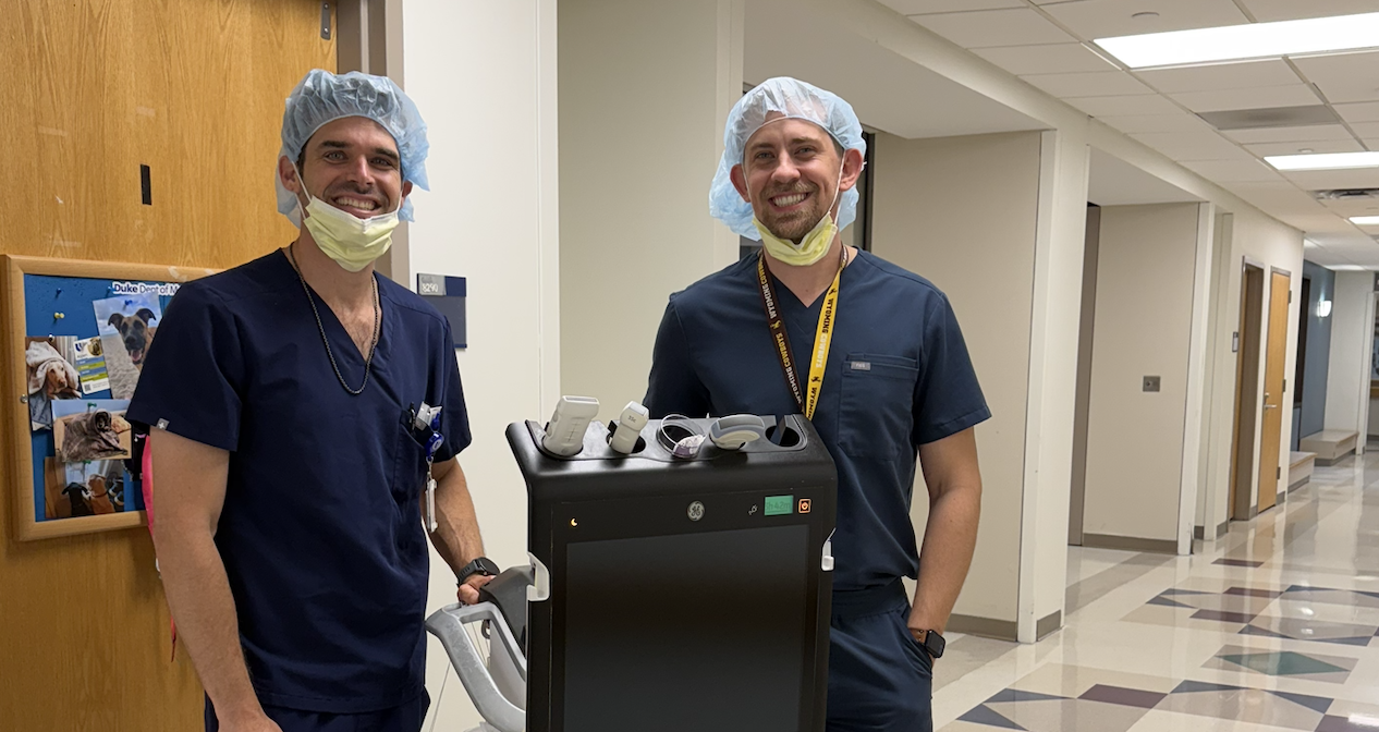 Residents smiling while standing in a hospital hallway next to medical equipment.