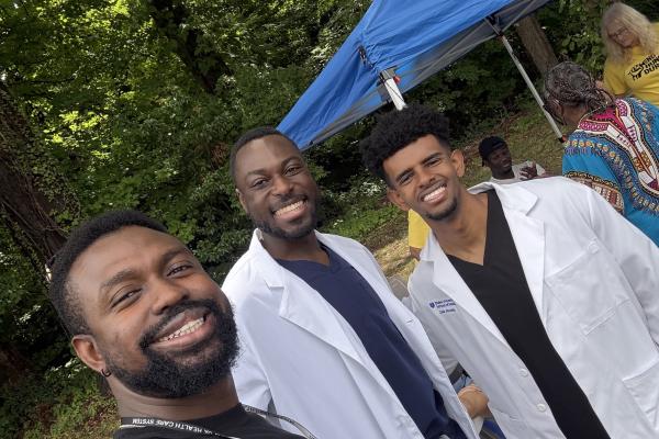 Residents in white coats standing outside near a blue tent. 