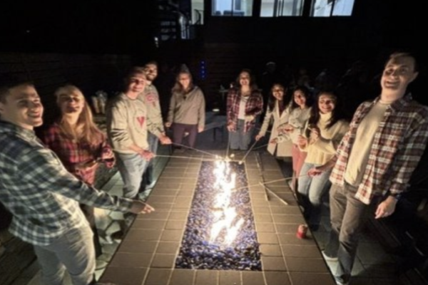 Residents gathered around a campfire roasting marshmellows. 