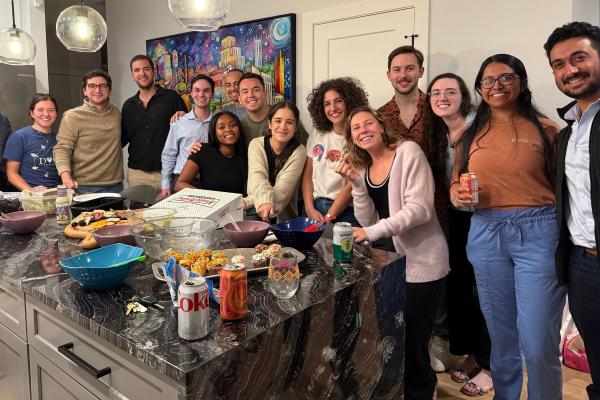 Residents in a large group hanging out in a kitchen setting with food. 