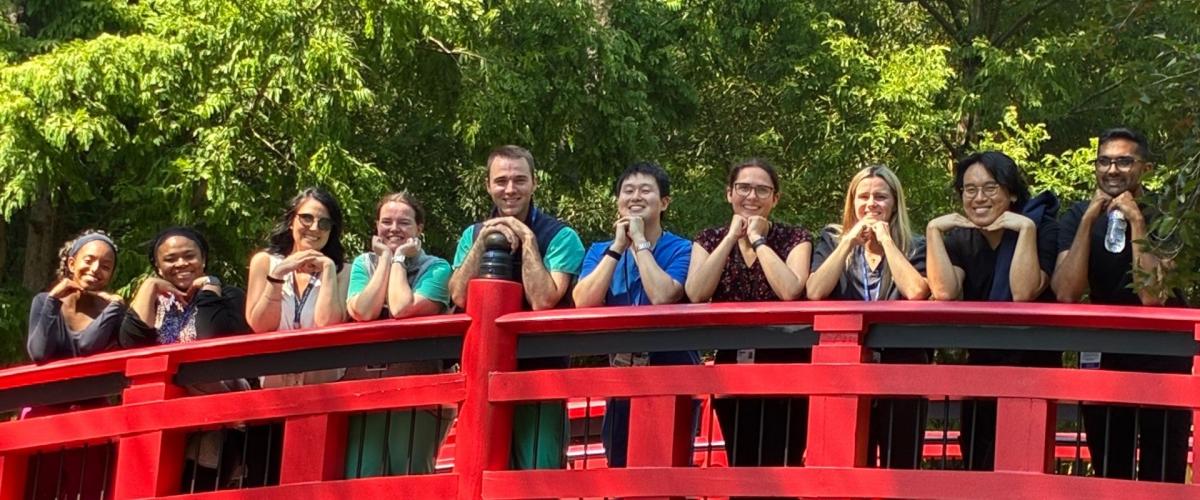 Residents smiling while standing on a bridge and resting their hands against their chins.