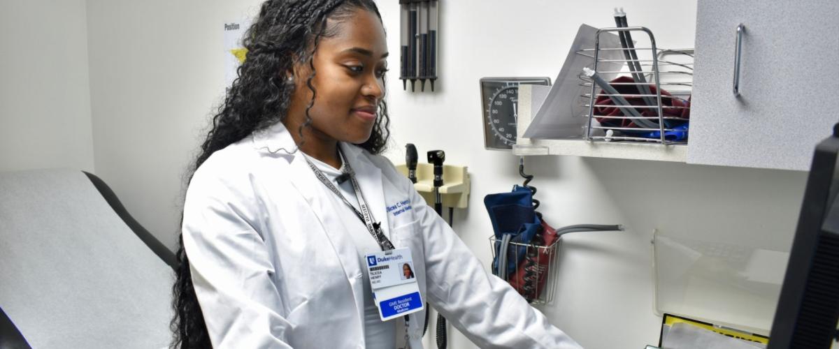 Resident in a patient care room looking at a computer screen smiling. 