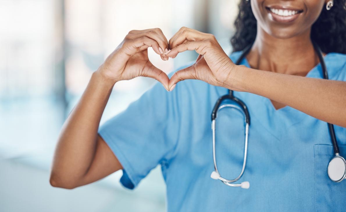 Closeup african american woman nurse making a heart shape with her hands while smiling and standing in hospital.