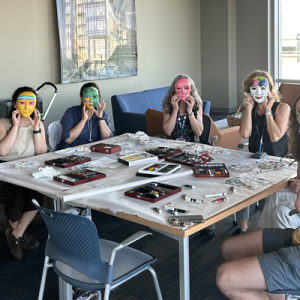 Students around a table with masks made during a crafting activity